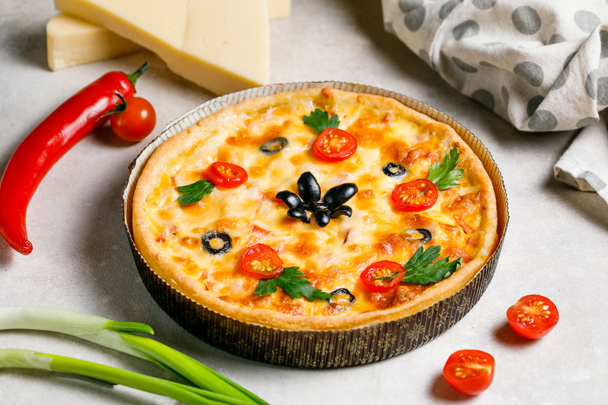 Пирог на песочном тесте с ветчиной, сыром и помидорами, украшен маслинами и зеленью